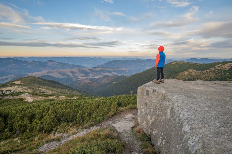 Young child boy hiker standing in mountains enjoying view of amazing mountain landscape